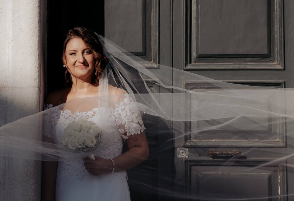 sposa con il velo davanti al portone di una cattedrale storica italiana durante il giorno del matrimonio
